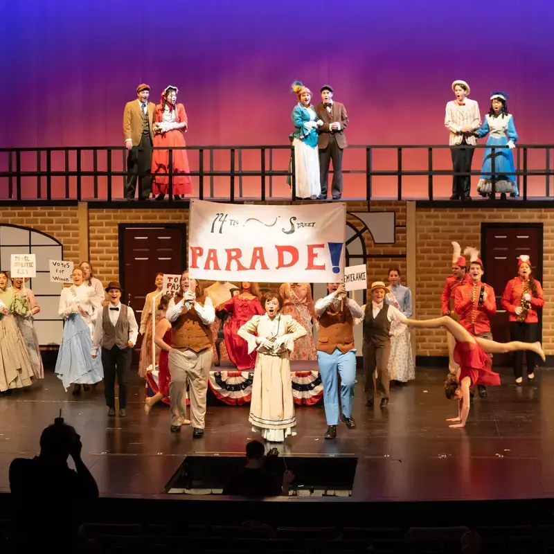 Loyola Academy theater students performing in a musical production under stage lights.