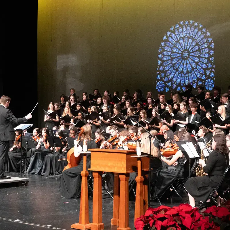 Loyola Academy choir, band, and orchestra students performing together on stage.