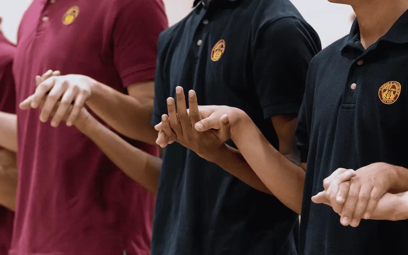 Loyola Academy students holding hands during the Sign of Peace at Mass, celebrating faith, community, and Jesuit values of love and unity.