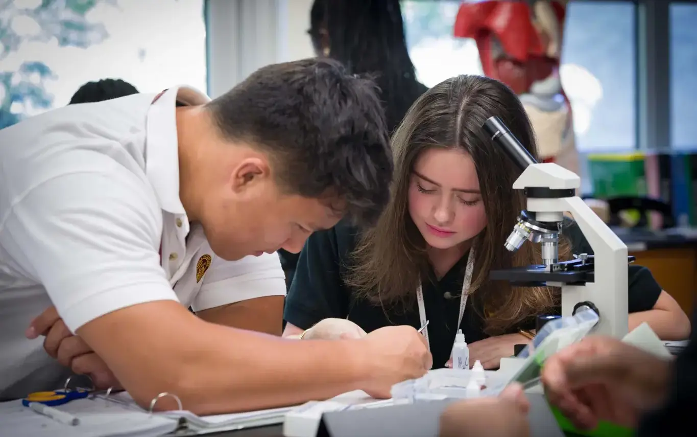 Loyola Academy students using a microscope during science class, exploring discovery and hands-on learning in a collaborative classroom setting.